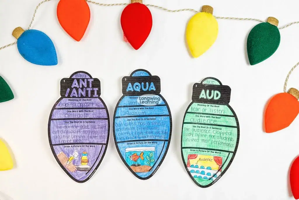 Christmas Greek and Latin roots activity display with three finished vocabulary ornaments arranged under a colorful string of holiday lights