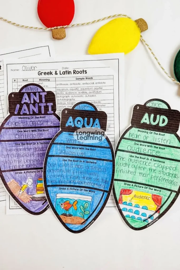 Flatlay image featuring finished Christmas Greek and Latin roots activity ornaments, worksheets, and holiday lights for a festive classroom vocabulary project.